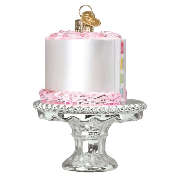 Cake on stand ornament at an angle, white frosting, pink piping, and a peek of rainbow layers
