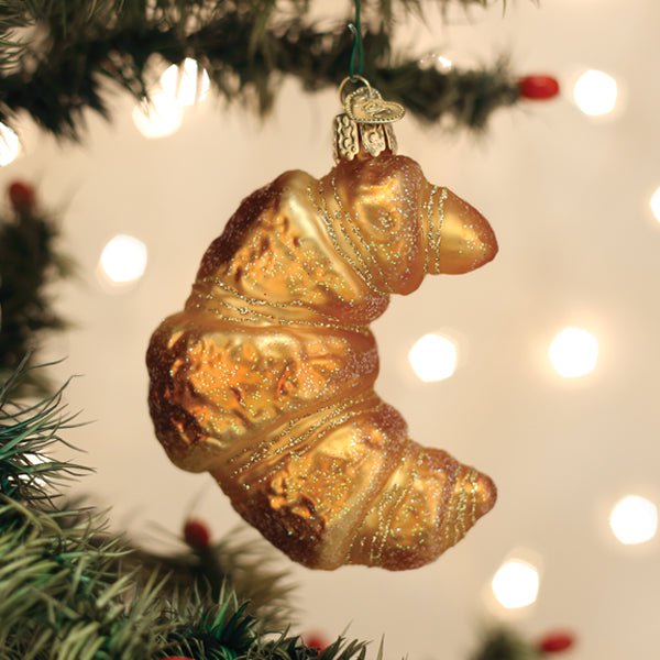 Croissant glass ornament hanging on a Christmas tree with soft bokeh lights for a pastry lover