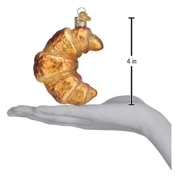 Croissant ornament resting on an open palm next to a 4 inch height marker for scale