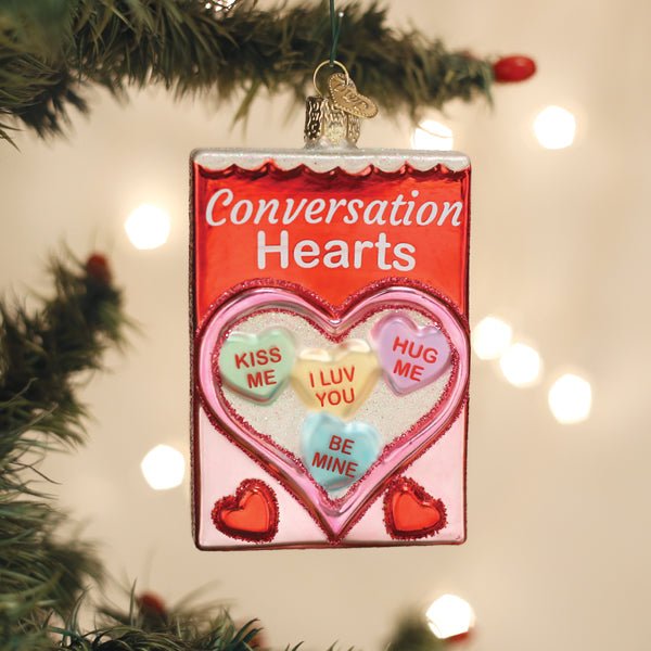 Conversation hearts candy box ornament hanging on a Christmas tree with warm bokeh lights