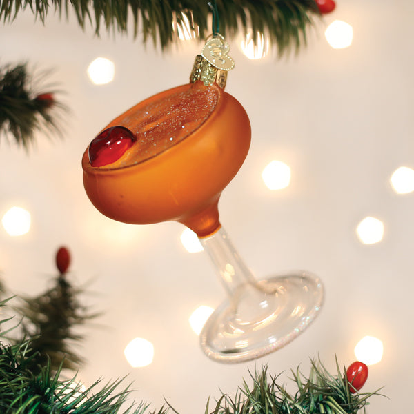 Manhattan cocktail glass ornament with cherries hanging on a lit Christmas tree