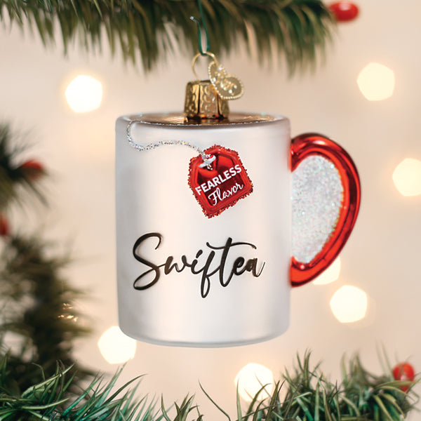 White Swiftea mug glass ornament with a red heart handle and tea tag, hanging on a Christmas tree