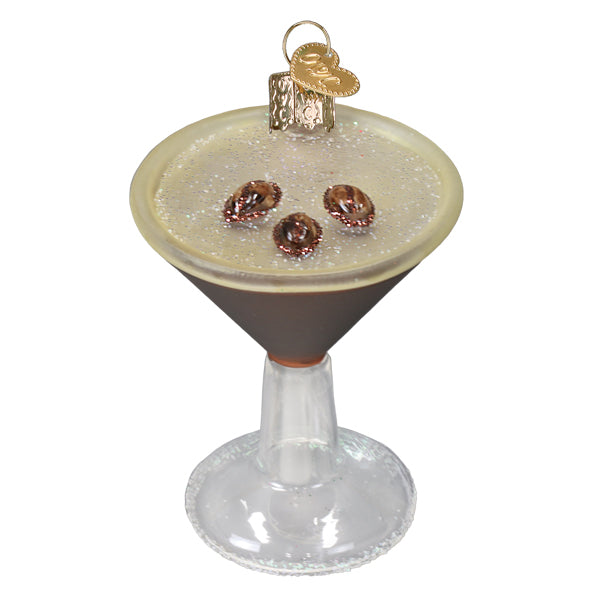 Espresso martini ornament with creamy foam and three coffee beans in a clear-stemmed glass, on white