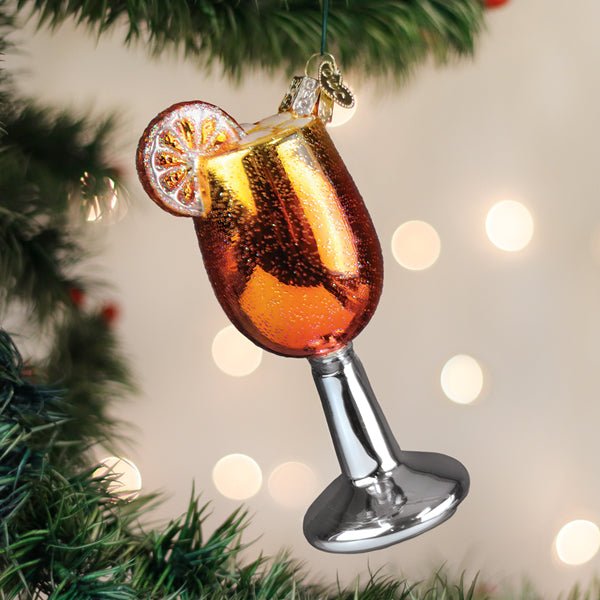 Orange Aperol Spritz glass ornament hanging on a lit Christmas tree with warm bokeh lights