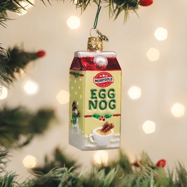 Eggnog carton glass ornament with a red top and Egg Nog lettering hanging on a lit Christmas tree