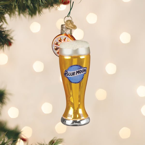 Blue Moon beer glass ornament hanging on a Christmas tree with warm twinkle lights behind it