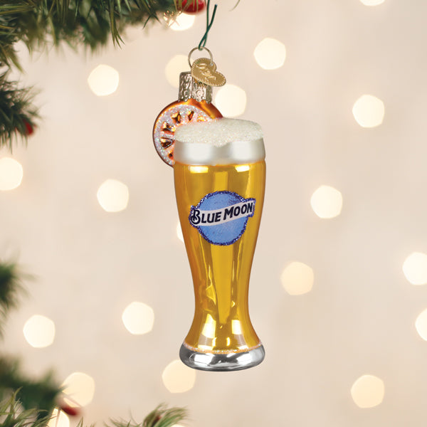 Blue Moon beer glass ornament hanging on a Christmas tree with warm twinkle lights behind it