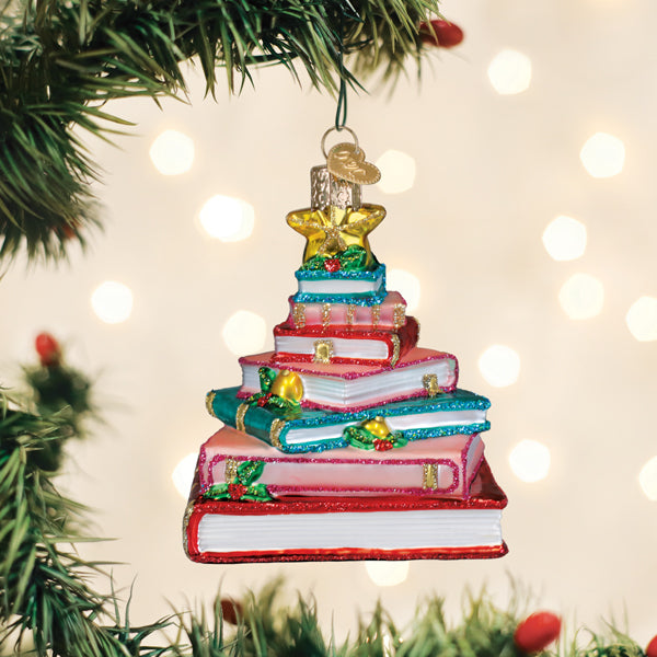 Book club tree glass ornament with holly and a gold star hanging on a lit Christmas tree