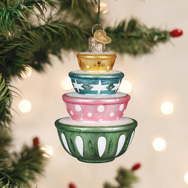 Stacked mixing bowls glass ornament hanging on a Christmas tree with warm bokeh lights behind it