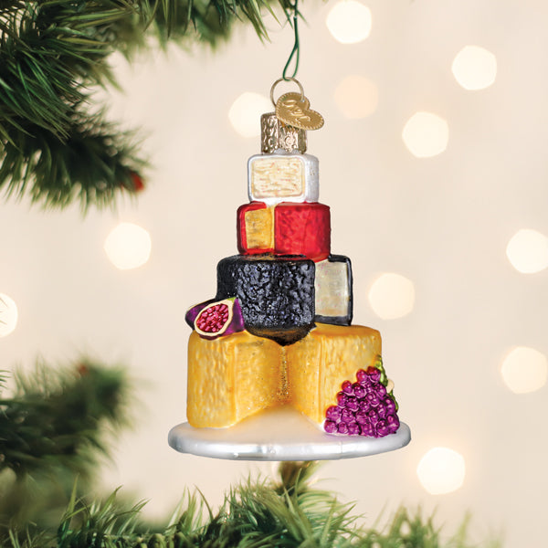 Stacked cheese tower ornament hanging on a Christmas tree branch above warm string lights
