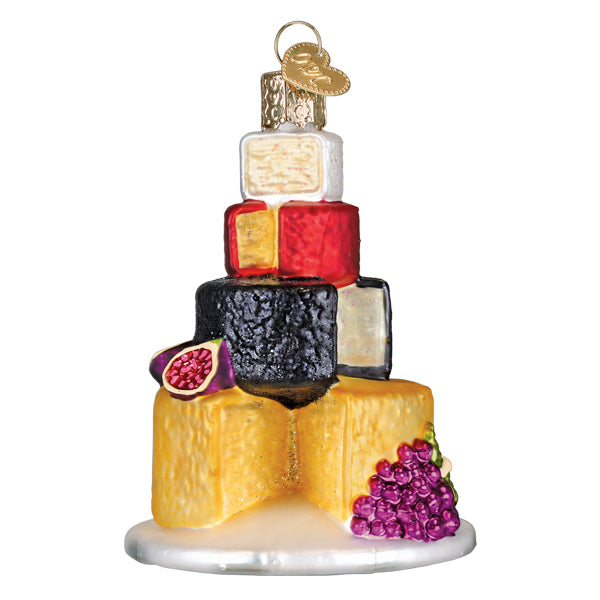 Cheese tower glass ornament stacked with yellow, black, red, and white wheels, figs, and purple grapes, on white