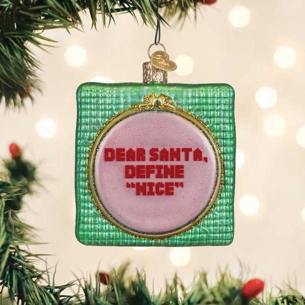 Dear Santa cross stitch hoop ornament hanging on a lit Christmas tree with warm bokeh lights