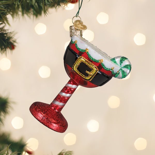 Red Santa cocktail glass ornament hanging on a lit Christmas tree with warm bokeh lights