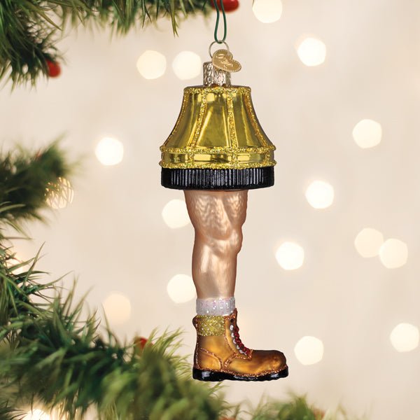 Man leg lamp ornament with a gold fringed shade hanging on a lit Christmas tree with warm bokeh
