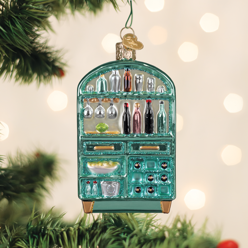 Bar cabinet glass ornament hanging on a Christmas tree branch with warm bokeh lights behind it