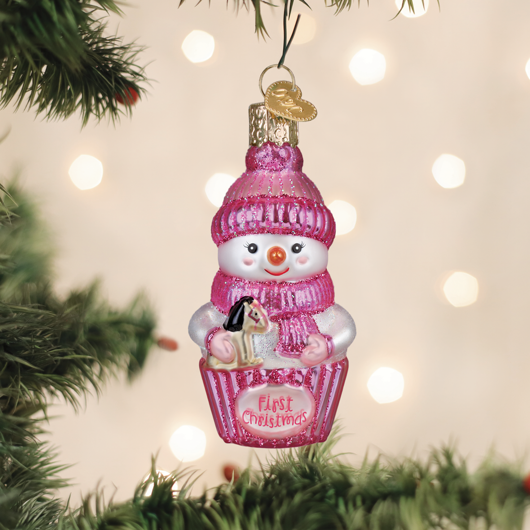 Pink snow baby first Christmas glass ornament hanging on a lit Christmas tree