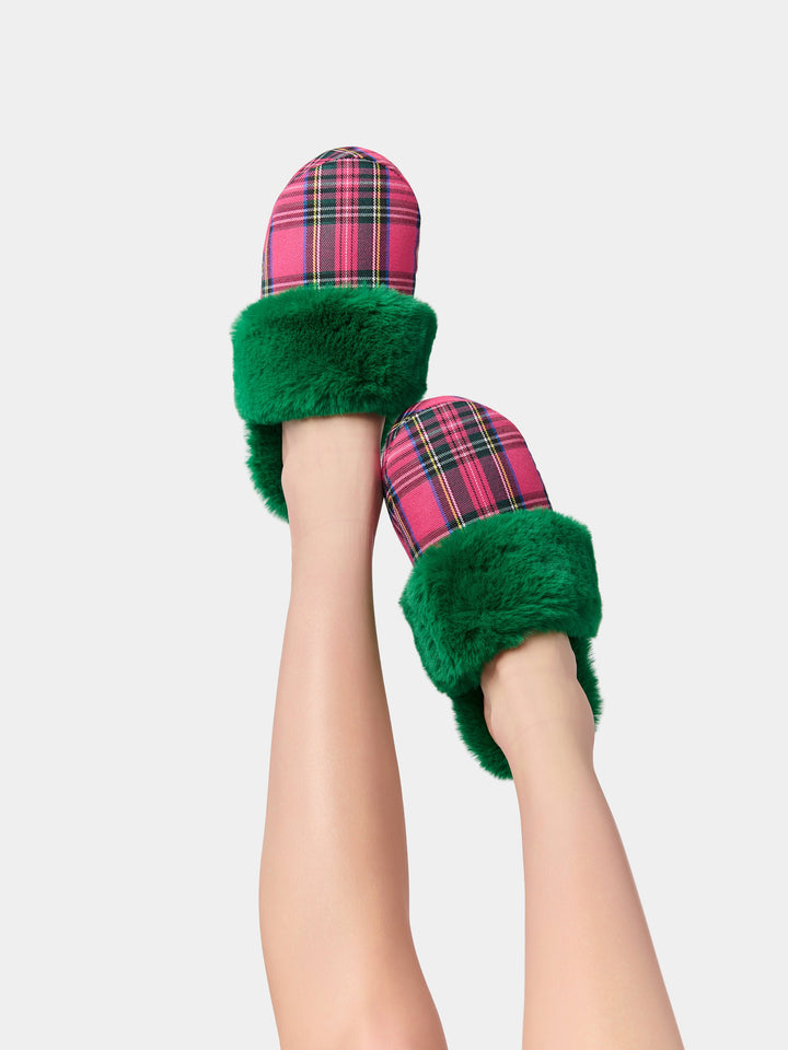 Legs raised wearing green faux fur slippers with red plaid