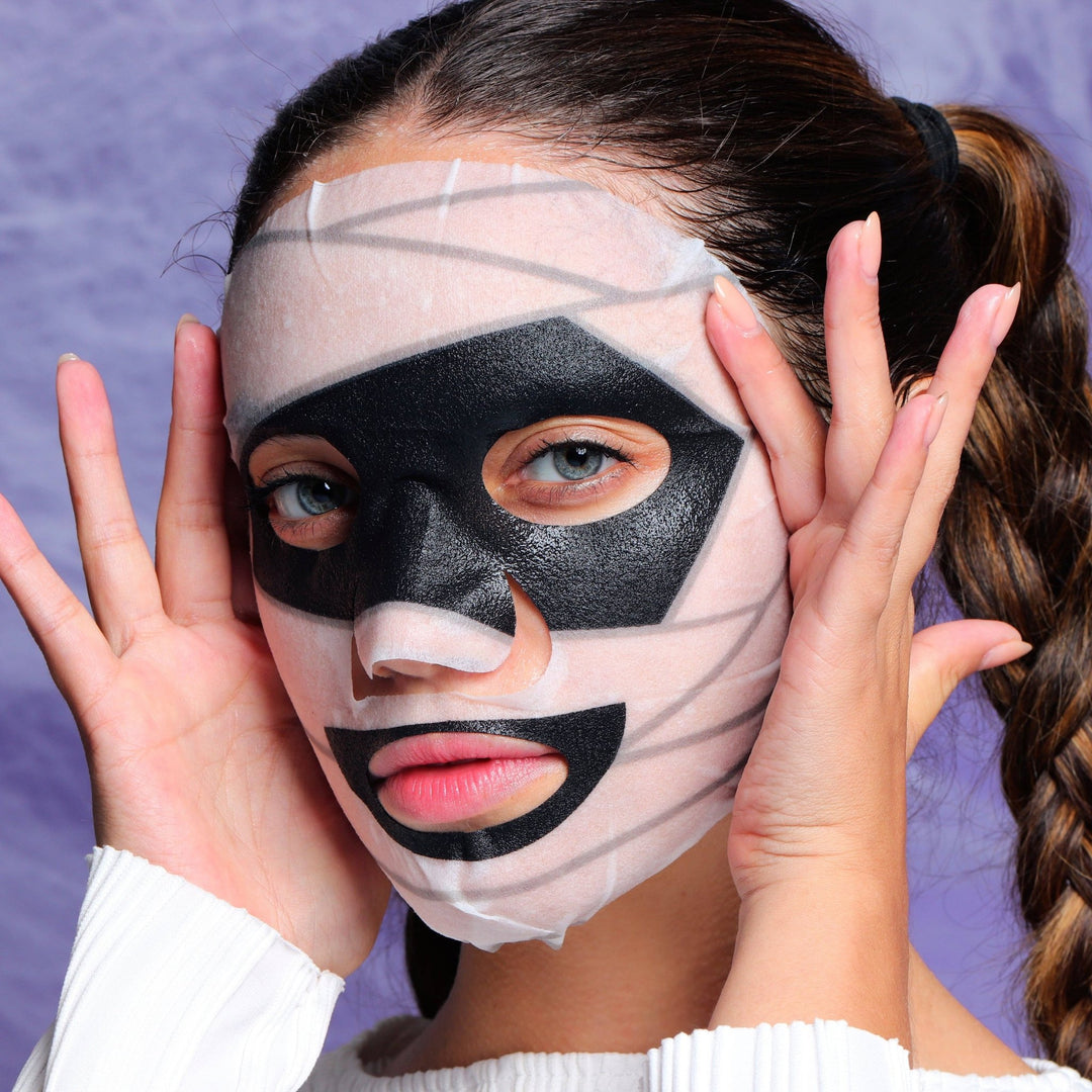 Model wearing the mummy printed sheet mask with black eye and mouth accents, spooky pampering for Halloween night
