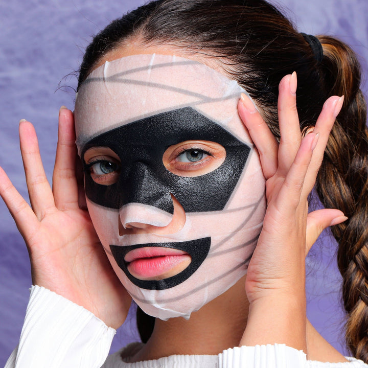 Model wearing the mummy printed sheet mask with black eye and mouth accents, spooky pampering for Halloween night