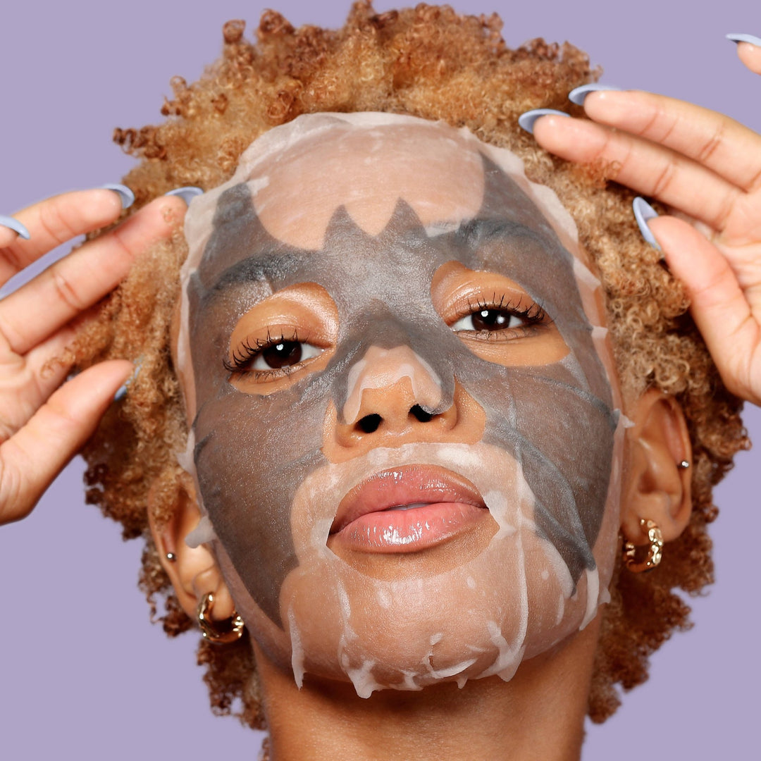 Model wearing the gray bat print charcoal sheet mask, detoxifying skincare for a Halloween spa night