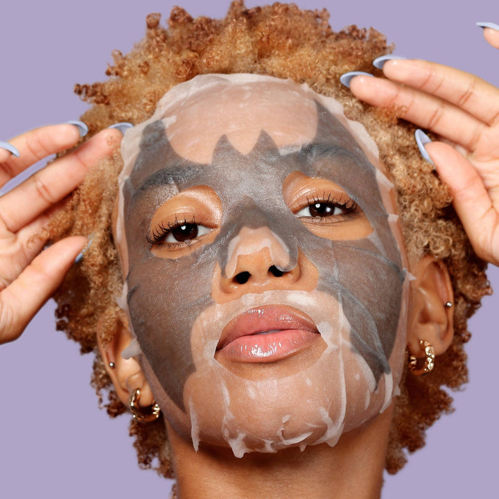 Model wearing the gray bat print charcoal sheet mask, detoxifying skincare for a Halloween spa night