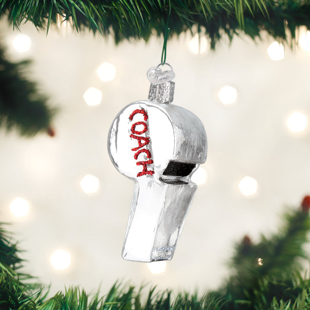 Coach's whistle ornament hanging on a lit Christmas tree with warm bokeh lights