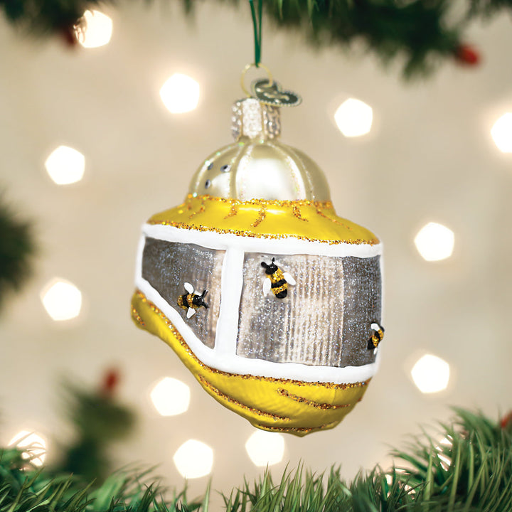 Beekeeper's hood bee Christmas ornament hanging on a tree branch with warm bokeh lights