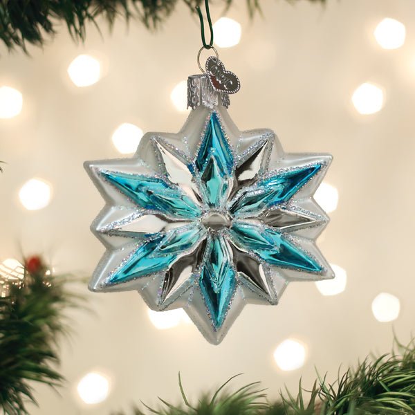 Blue and silver snowflake glass ornament hanging on a lit Christmas tree