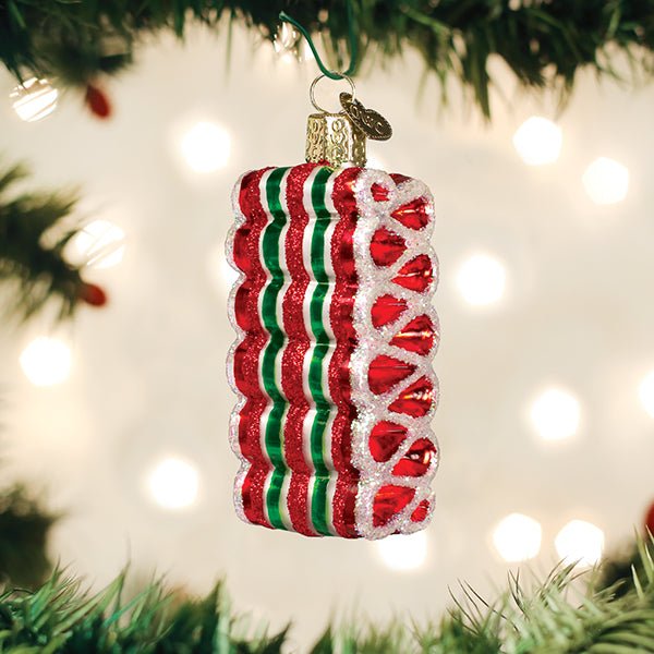 Ribbon candy glass ornament hanging on a Christmas tree with warm twinkle lights behind it