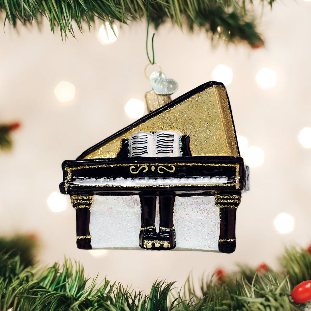 Black baby grand piano glass ornament with a gold lid and sheet music, hanging on a Christmas tree