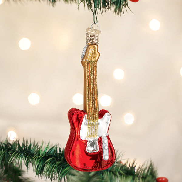 Red electric guitar Christmas ornament hanging on a tree branch with warm bokeh lights