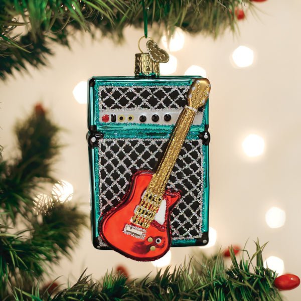 Red guitar and teal amp ornament hanging on a lit Christmas tree with warm bokeh lights