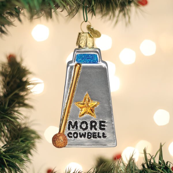 Silver cowbell glass ornament lettered More Cowbell with a gold drumstick, hanging on a Christmas tree