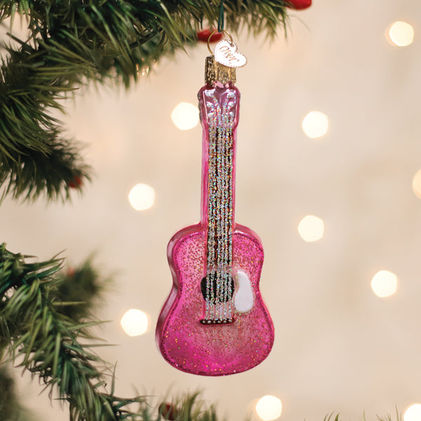 Pink glitter guitar Christmas ornament hanging on a tree branch with warm bokeh lights