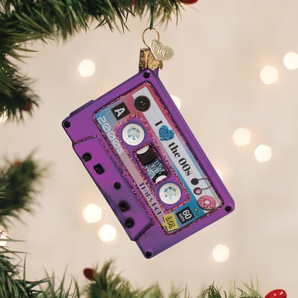 Purple 00s cassette tape ornament hanging on a lit Christmas tree with warm bokeh lights