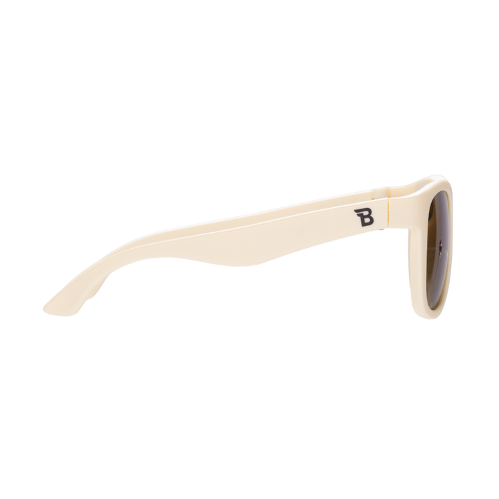Side profile of cream aviator kids sunglasses showing the flexible temple arm and Babiators logo.