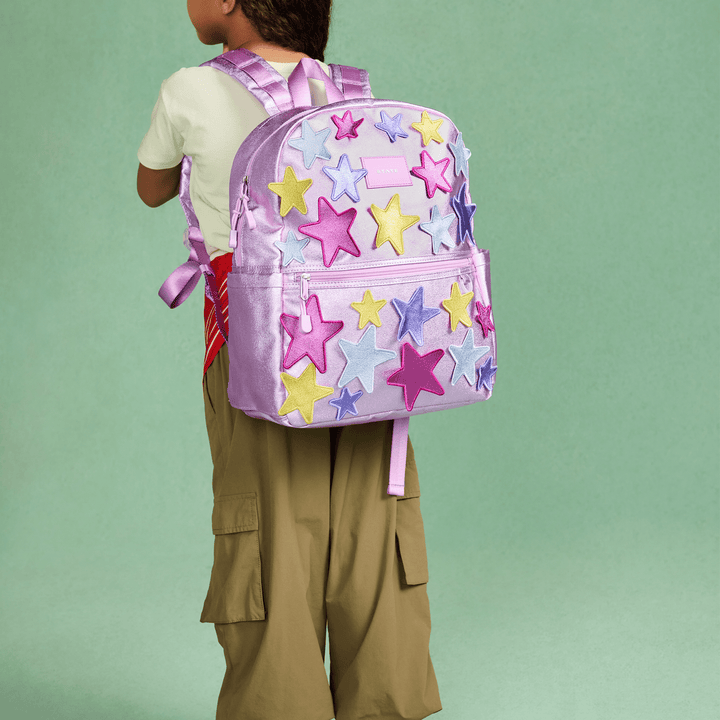 Child wearing the lilac 3D Stars STATE Kane backpack against a green backdrop
