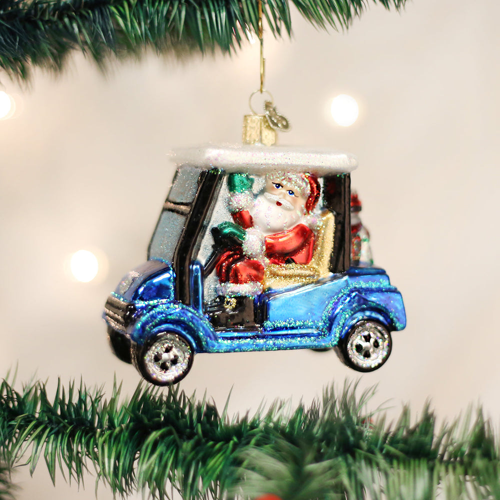 Golf cart Santa ornament hanging on a Christmas tree with glowing lights behind