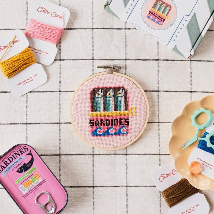 Sardines cross stitch hoop with thread cards, scissors, and sardine tin in a flat lay