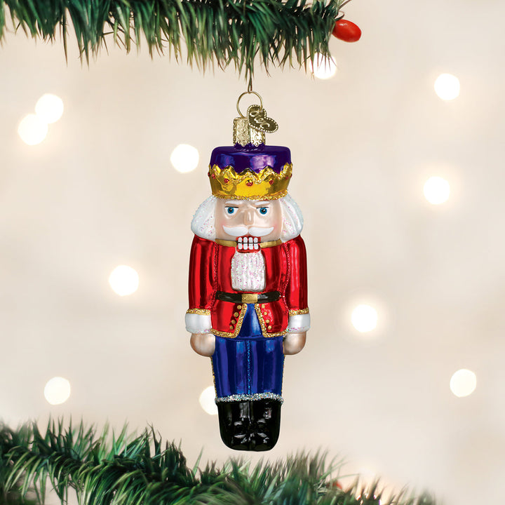 Nutcracker Prince glass ornament hanging on a lit Christmas tree