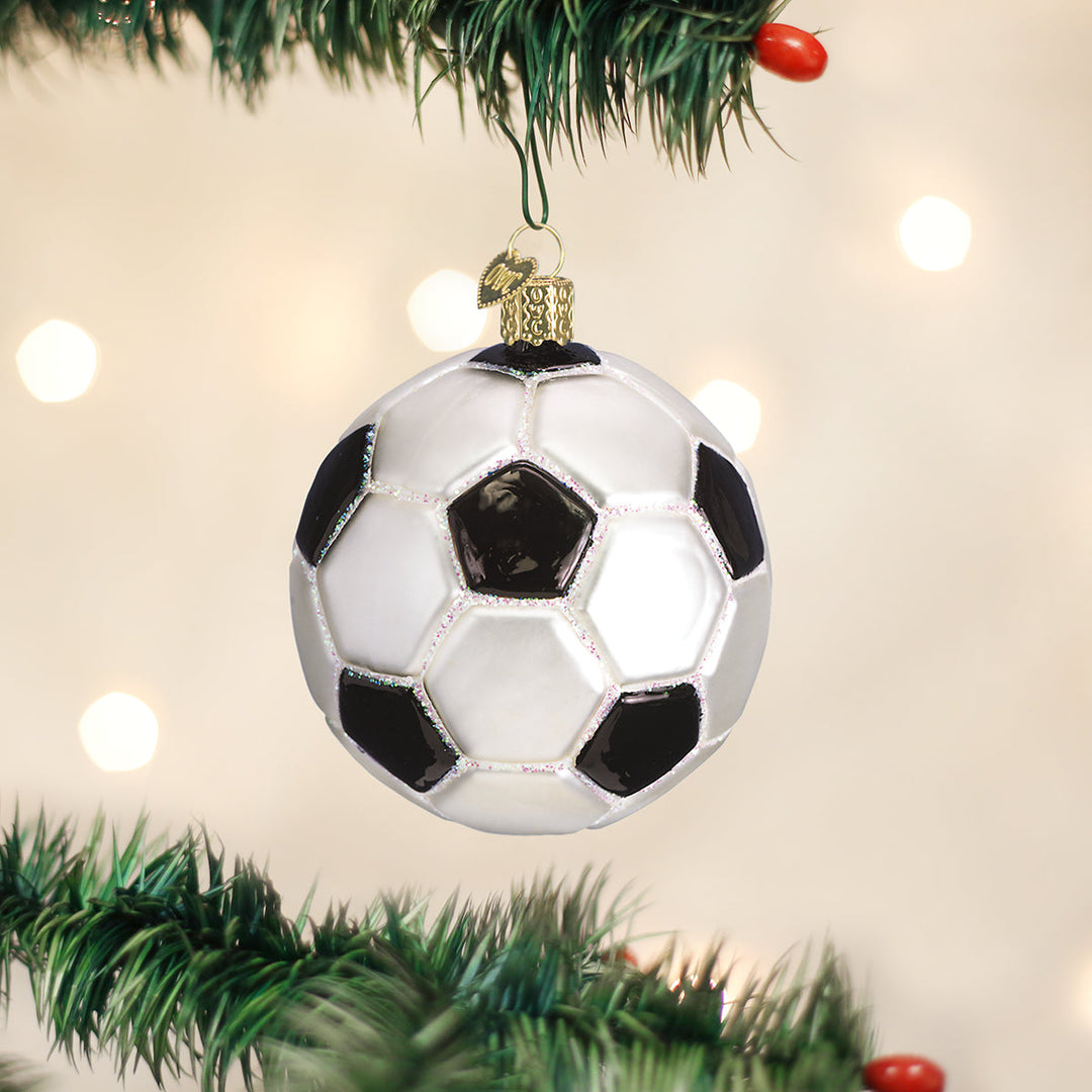 Soccer ball Christmas ornament hanging on a pine branch with soft holiday lights behind