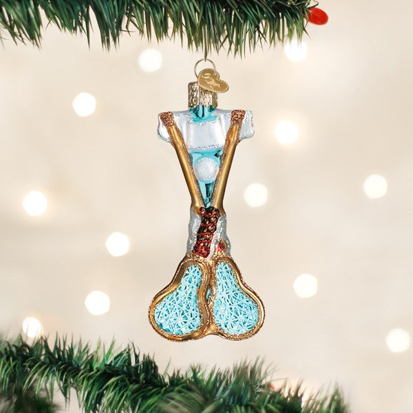 Lacrosse sticks Christmas ornament hanging from a pine branch with warm lights in the background
