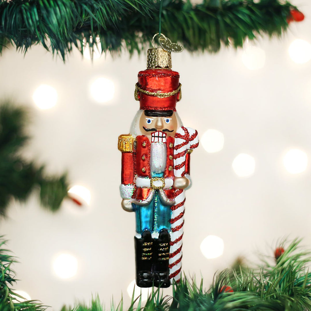 Peppermint nutcracker glass ornament with a candy cane hanging on a lit Christmas tree