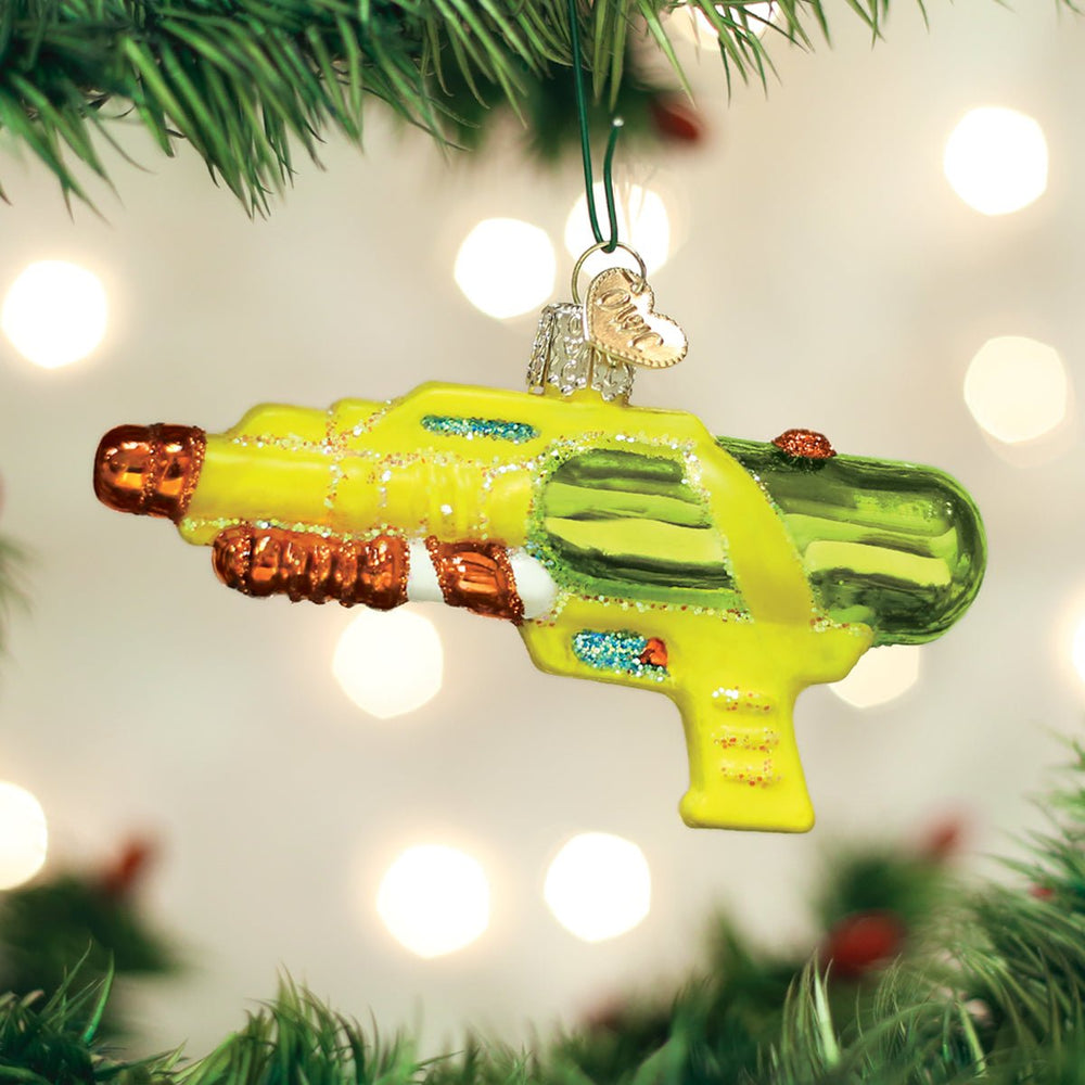 Yellow and green squirt gun ornament hanging on a lit Christmas tree with warm bokeh lights