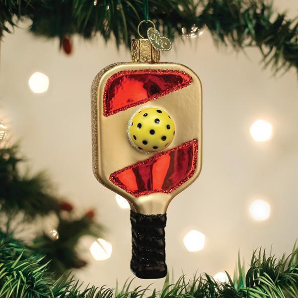 Pickleball paddle glass ornament with a yellow ball hanging on a lit Christmas tree