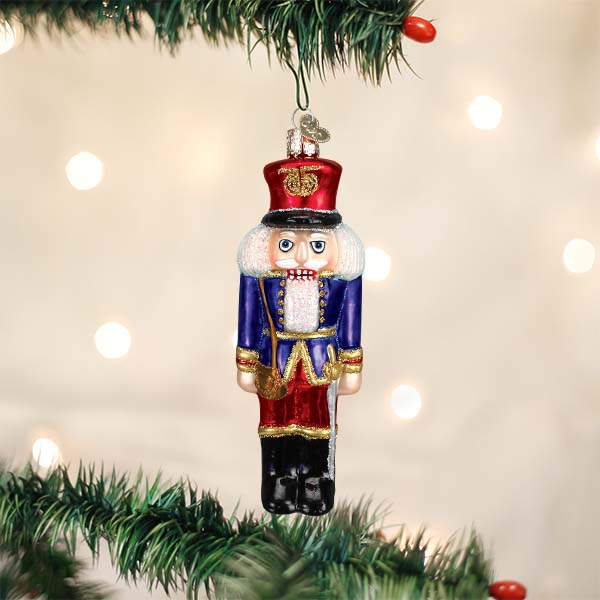 Blue coat nutcracker soldier glass ornament hanging on a lit Christmas tree