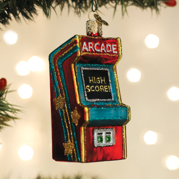 Red and blue arcade game ornament hanging on a lit Christmas tree with soft holiday lights