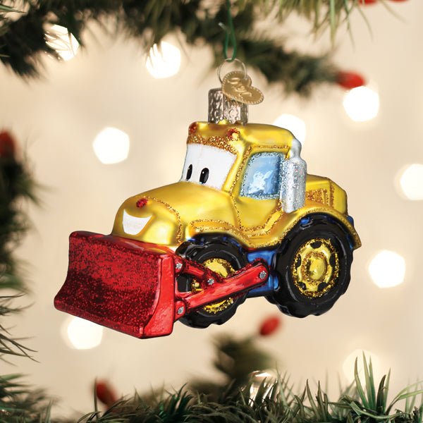 Yellow bulldozer ornament hanging on a lit Christmas tree with warm bokeh lights