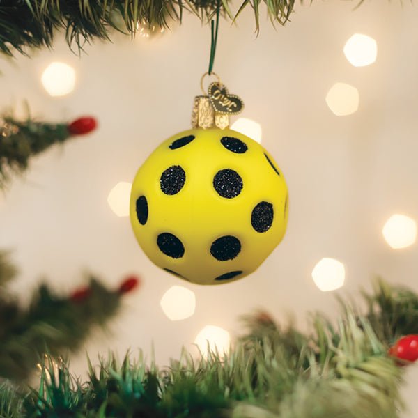Yellow pickleball ornament hanging on a lit Christmas tree with warm bokeh lights