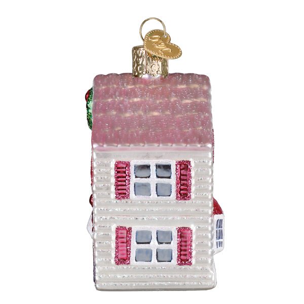 Side view of the dollhouse ornament with a glittered pink roof and shuttered windows, on white